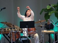 2025 Susie Ibarra stands onstage holding two tiny gold bells